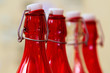 three glass bottles of red color and one transparent, with reusable corks on an iron bracket stand in a row, focus in the foreground on the first bottle of red color