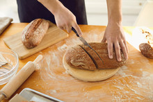 Hands Cutting Fresh Homemade Bread On A Table In A Bakery Kitchen.