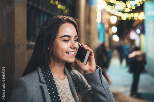 Fotomural Young smile woman calling mobile phone on background bokeh light in night europe city