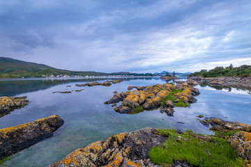 Wall Mural - Sunset seascape with rocks in water and Skye island at the background. Hebrides archipelago, Scotland.