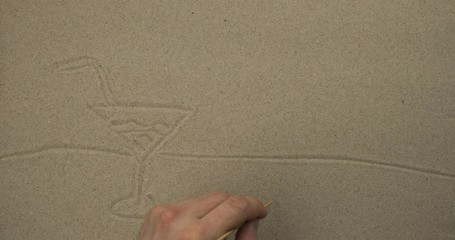 Wall Mural - Drawing with a stick on the sand. Cocktail glass on the beach against the background of the sun and seagulls.