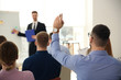 © New Africa - Man raising hand to ask question at business training indoors