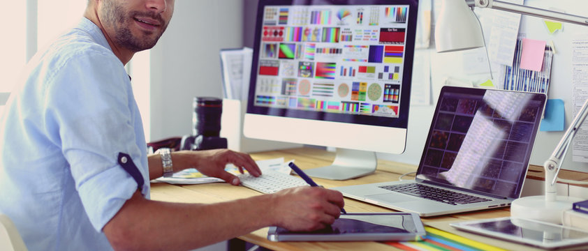 Portrait of young designer sitting at graphic studio in front of laptop and computer while working online.