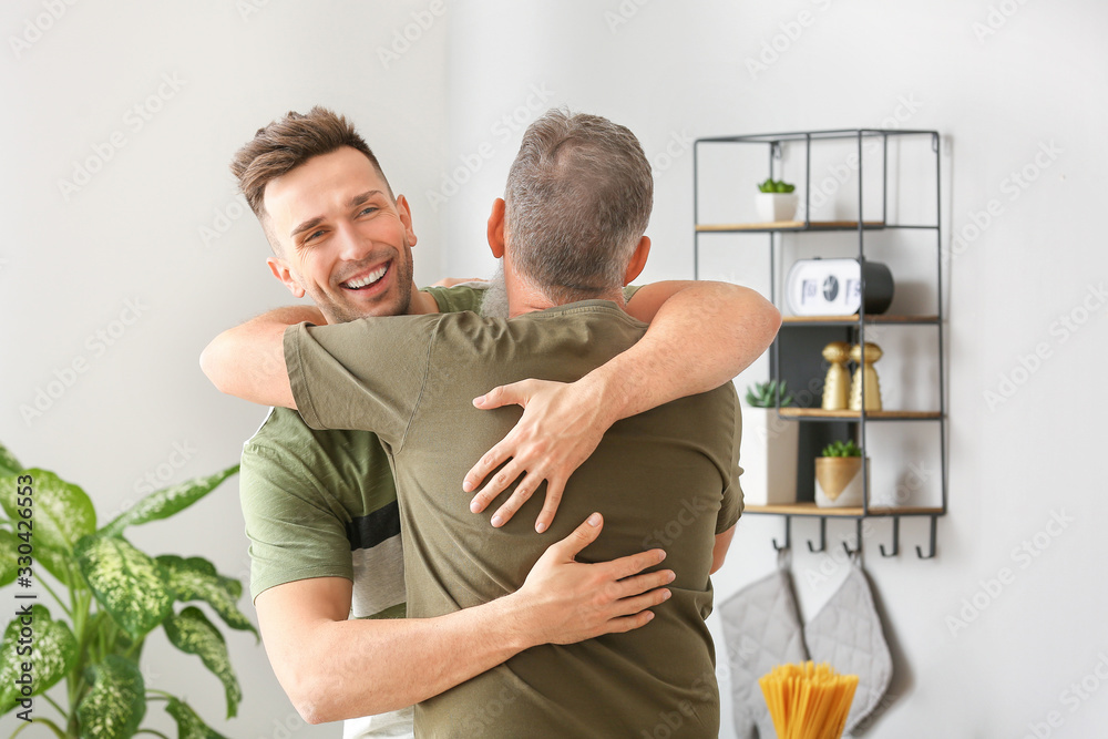 Senior man and his adult son hugging in kitchen