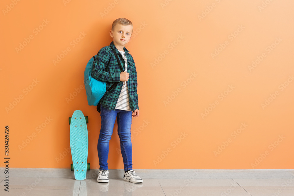 Cute little boy with skate and backpack near color wall