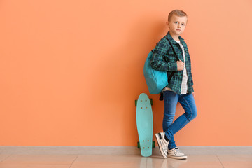 Cute little boy with skate and backpack near color wall