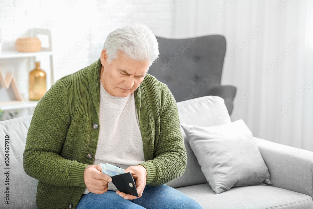 Sad senior man with purse at home
