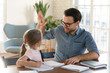 © fizkes - Happy young dad giving high five to smiling little daughter, satisfied with homework. Joyful male tutor praising small girl with successful exercise finish. Home schooling children education concept.
