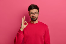 No Problem Concept. Bearded Man Makes Okay Gesture, Has Everything Under Control, All Fine Gesture, Wears Spectacles And Jumper, Poses Against Pink Background, Says I Got This, Guarantees Something