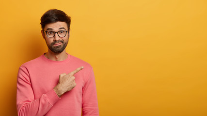 Wall Mural - Surprised cheerful unshaven man advices special discount offer, points at upper right corner to advertise product, poses against yellow background, dressed casually, shows promo, invites you to party