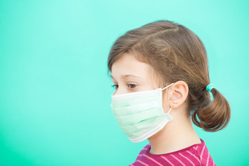 Sad little girl in a green protective disposable medical mask on a green background. Coronavirus Protection Concept, COVID-19. Pandemic 2020