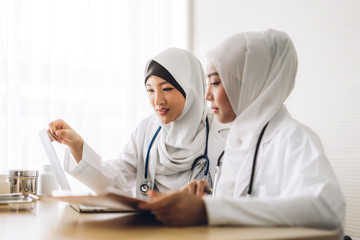 Wall Mural - Two muslim asian woman doctor working with clipboard and laptop computer on desk in hospital.healthcare and medicine