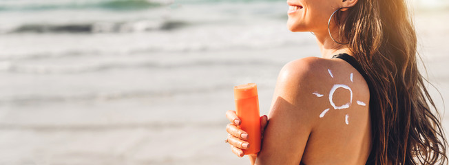 Woman wearing two piece bikini applying suncream with sun drawn on back and holding sunscreen lotion on the tropical beach.Young girl with sun block skin protection.Summer vacations