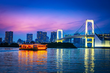 Canvas Print - Japan. Tokyo. Odaiba island. The rainbow bridge glows at night. The ship floats on Tokyo Bay. Tours of Tokyo at night. Rainbow bridge on the background of the night city. Vacations in Japan.