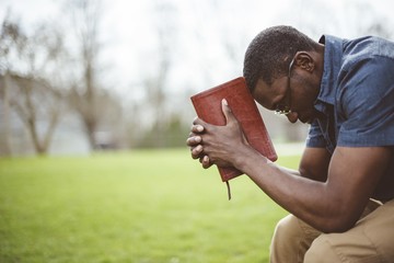 Young African-American male sitting with closed eyes with the Bible in his hands