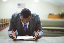 African-American Male Praying With His Head Down Looking At The Bible At The Church