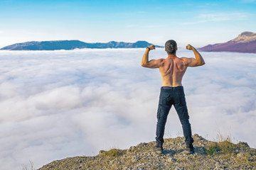 young man of athletic build stands on the top of a mountain demonstrating male power and strength