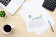 © satapatms - Wood office desk table with business financial charts documents, calculatoe, laptop computer, cup of coffee and supplies. Top view, flat lay.