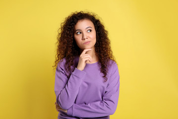 Pensive African-American woman on yellow background. Thinking about difficult question