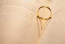 Warm Light Cast Golden Ring Shadow On Open Book With Shallow Depth Of Field
