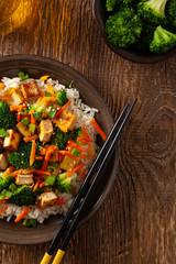 Wall Mural - Tofu with rice and vegetables. Served on brown plate with chopsticks. Top view.