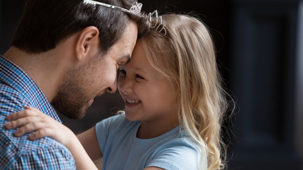 Wall Mural - Overjoyed little preschooler girl child touch foreheads look in eyes playing with loving young dad wearing toy crown, happy father and small daughter have fun playing together funny games at home