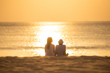 Wall Mural - couple sit on sand looking sunset in sea together.