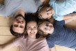© fizkes - Top view close up portrait of happy young family with little children lying on warm wooden floor posing for picture together, smiling parents and small kids relaxing at home look at camera