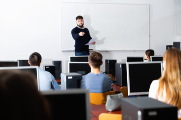 Wall Mural - Friendly male teacher lecturing attentive adult students in computer room