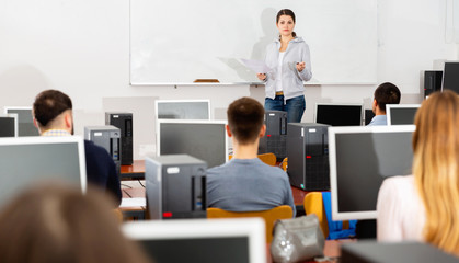 Wall Mural - Young female trainer giving presentation to adult audience in computer class