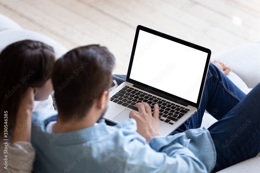 Loving couple looking at laptop screen blank white mockup close up, sitting on cozy sofa, young man and woman reading email, message, searching information in internet, shopping or chatting online - obrazy, fototapety, plakaty 