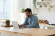 © fizkes - Smiling young man working on laptop in modern kitchen, checking email in morning, writing message in social network, happy young male using internet banking service, searching information