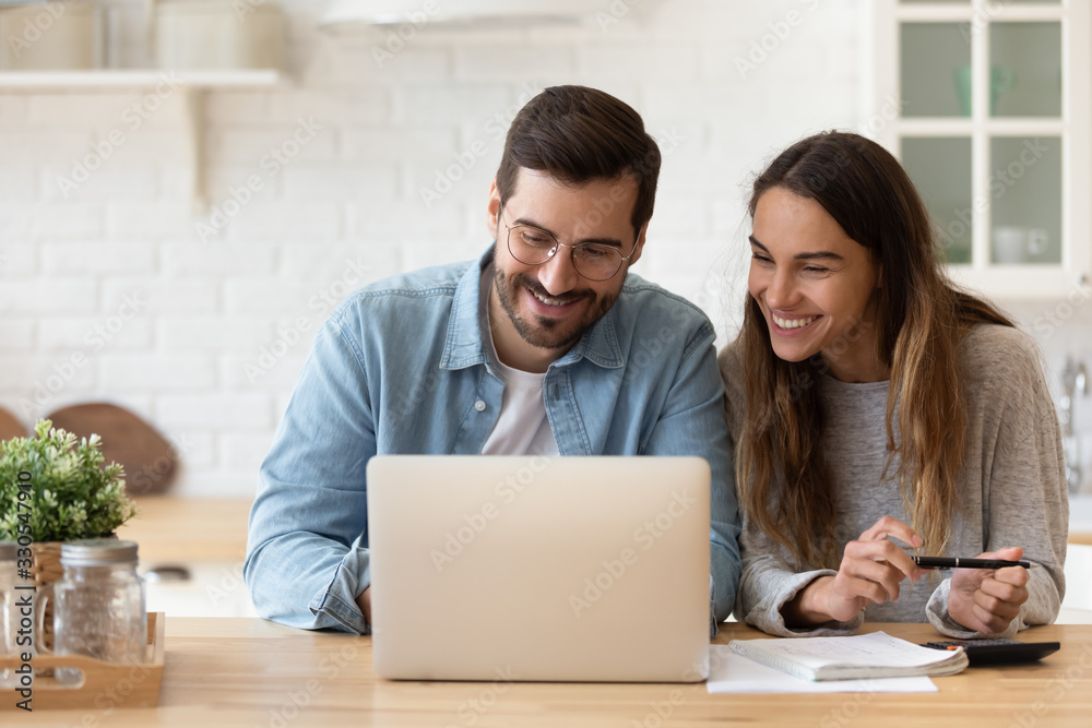 Happy young couple planning budget, reading good news in email, refund or mortgage approval, smiling woman and man looking at laptop screen, checking finances, sitting at table at home together - obrazy, fototapety, plakaty 