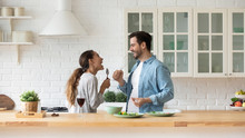 Happy Loving Couple Singing Song And Dancing, Having Fun With Kitchenware In Kitchen, Funny Excited Wife And Husband Holding Whisk And Spoon, Listening To Music, Preparing Food Together