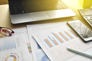 Financial graphs and charts with eyeglasses, calculator on desk.