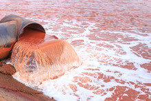 Rusty Red Water Drains From A Pipe Into A Red Lake