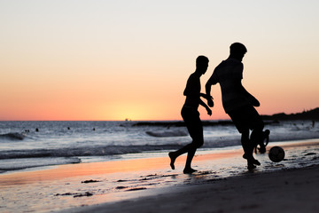 Two boys playing soccer in the beach at sunset