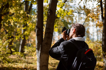 Canvas Print - Young man photographer in jacket with backpack in forest taking pictures of nature