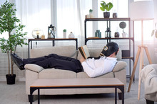 Pandemic Coronavirus Quarantine Period Concept. National Quarantine Concept. A Man In A Gas Mask Lies On A Sofa And Reads A Book. Stay At Home Idea.