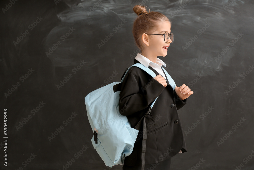 Cute little schoolgirl near blackboard in classroom