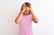 Young redhead woman wearing striped casual t-shirt stading over white isolated background suffering from headache desperate and stressed because pain and migraine. Hands on head.