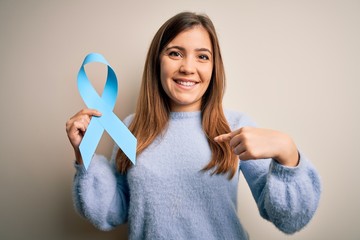 Sticker - Young blonde woman holding prostate cancer awareness campaing blue ribbon with surprise face pointing finger to himself