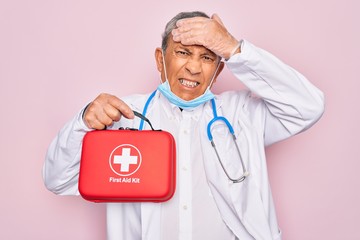 Canvas Print - Senior handsome hoary doctor man wearing stethoscope and medical mask holding first aid kit stressed with hand on head, shocked with shame and surprise face, angry and frustrated. Fear and upset