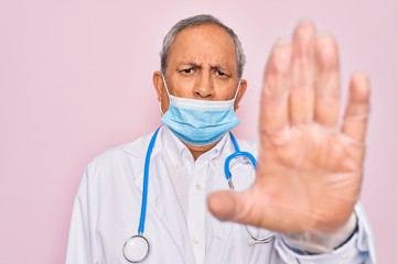 Sticker - Senior hoary doctor man wearing medical mask and stethoscope over pink background with open hand doing stop sign with serious and confident expression, defense gesture