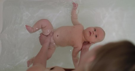 top view of newborn baby boy swimming during bathing with mother's help