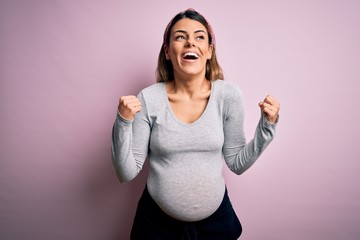 Sticker - Young beautiful brunette woman pregnant expecting baby over isolated pink background celebrating surprised and amazed for success with arms raised and open eyes. Winner concept.