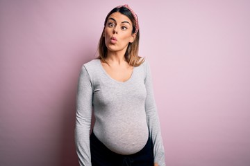 Sticker - Young beautiful brunette woman pregnant expecting baby over isolated pink background making fish face with lips, crazy and comical gesture. Funny expression.