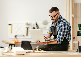 Carpenter using laptop in workshop.