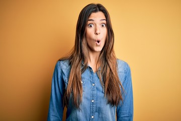 Wall Mural - Young beautiful girl wearing casual denim shirt standing over isolated yellow background afraid and shocked with surprise expression, fear and excited face.