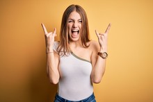 Young Beautiful Redhead Woman Wearing Casual T-shirt Over Isolated Yellow Background Shouting With Crazy Expression Doing Rock Symbol With Hands Up. Music Star. Heavy Music Concept.
